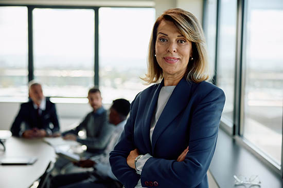 Smiling mature businesswoman with arms crossed at meeting room looking at camera.
